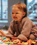 En bebis sitter på golvet omgiven av färgglada dominobrickor