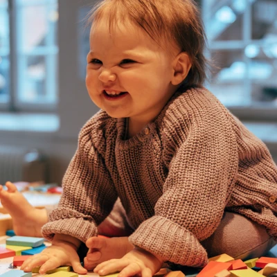 En bebis sitter på golvet omgiven av färgglada plattor