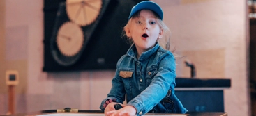 A little girl sitting at a table in front of a clock.