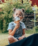 A little girl sitting on the ground eating an ice cream cone.