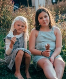 Two little girls sitting on the ground eating ice cream.