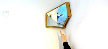 A woman reaching up to a mirror on the wall.