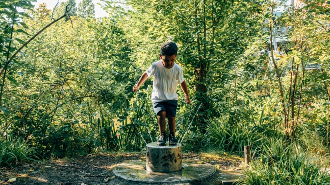 En pojke står uppe på en cylinder i skogen.