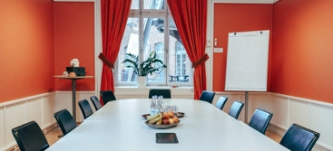 A conference room with a white table, red walls and black chairs.