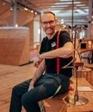 A smiling man sitting on top of a wooden table.