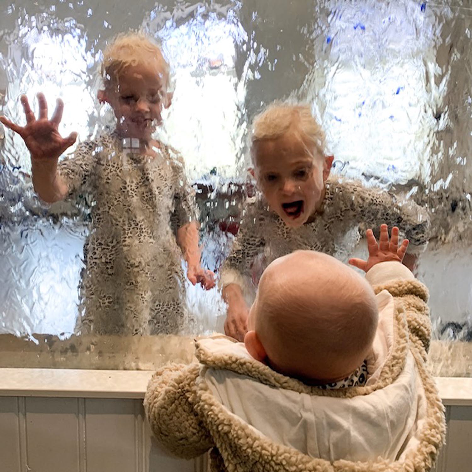 Tre barn tittar på varandra genom en glasskiva