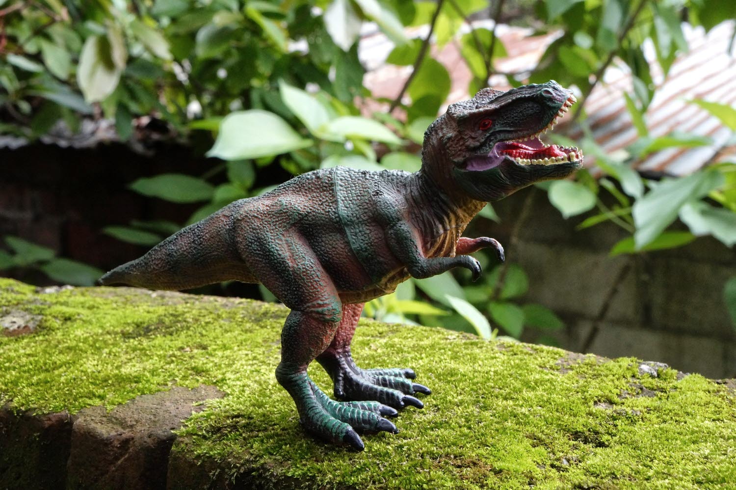 En leksaksdinosaurie som står bland mossa och gröna blad
